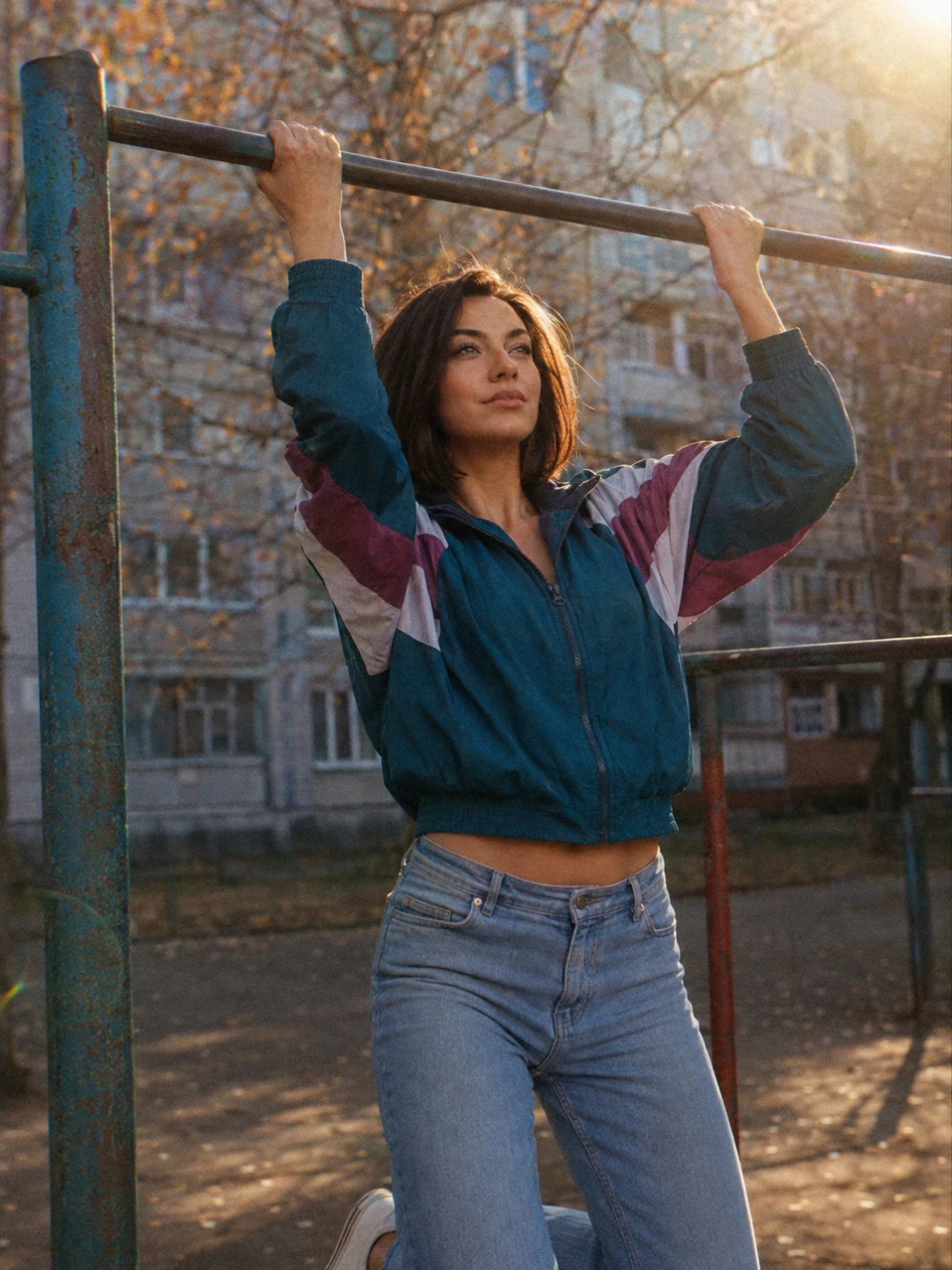Молодая женщина висит на турнике на спортивной площадке советского двора